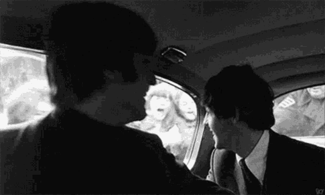 a black and white photo of two men sitting in a car talking to each other .