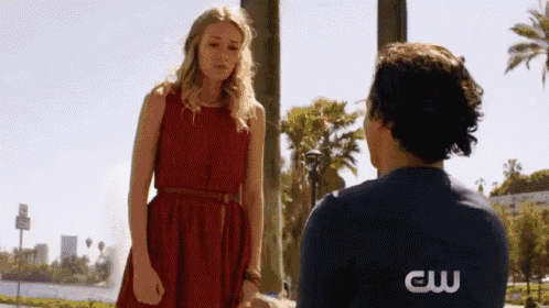 a woman in a red dress stands next to a man in a blue shirt with the letters cw on his back