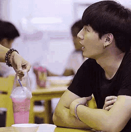 a man is sitting at a table with his arms crossed and a woman is giving him a drink with a straw