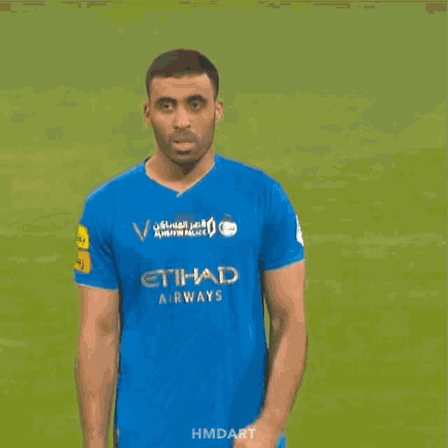 a man wearing a blue etihad airway jersey is standing on a soccer field