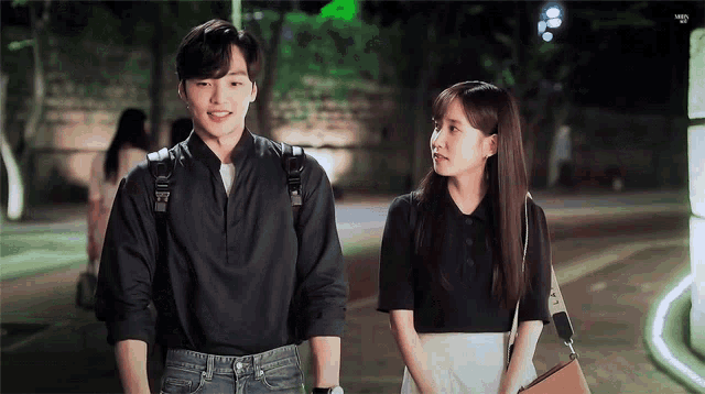 a man and a woman are standing next to each other on a sidewalk at night .