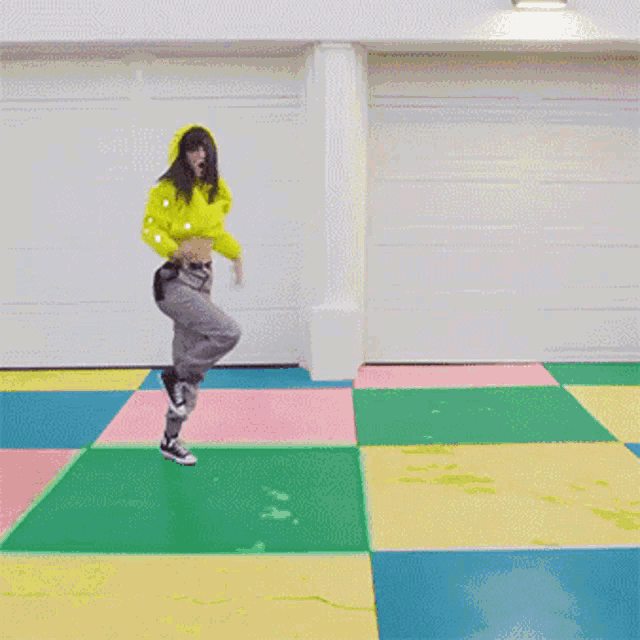 a woman in a yellow hoodie is dancing on a multicolored floor