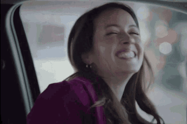 a woman is sitting in the back seat of a car laughing with her eyes closed .