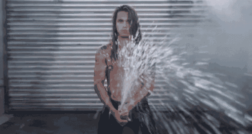 a man with long hair is standing in front of a hose spraying water .