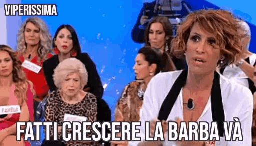 a woman is sitting in front of a group of women with the words fatti crescere la barba va written above her .