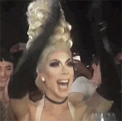 a drag queen is wearing a black hat and smiling while standing in a crowd .