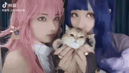two girls in cosplay are holding a cat in their arms .