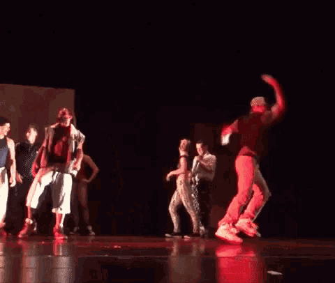a group of people dancing on a stage with red lights behind them