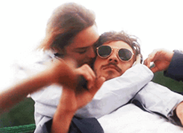 a woman is kissing a man wearing sunglasses on the cheek