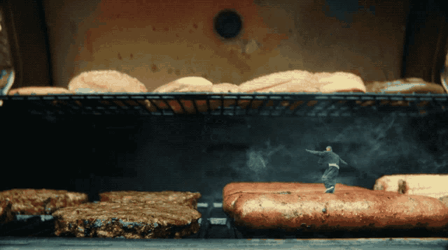a man standing on top of a grill with hamburgers and hot dogs