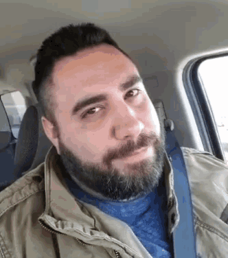 a man with a beard is sitting in a car with a seat belt .