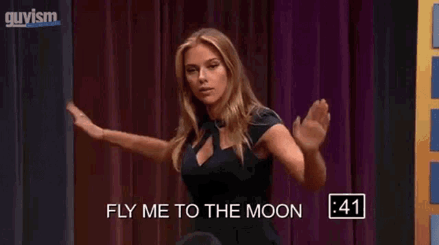 a woman in a black dress is dancing on a stage with the words fly me to the moon on the screen .