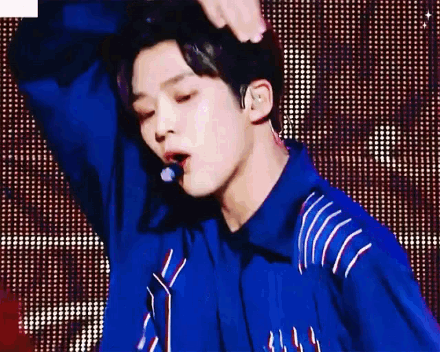 a young man wearing a blue shirt and tie is standing on a stage with his arms outstretched .