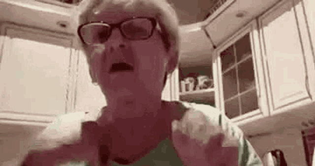 an older woman wearing glasses is standing in a kitchen .