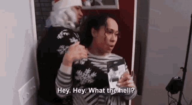 a man in a santa hat is standing next to a woman in a sweater and talking to her .