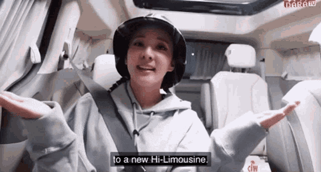 a woman wearing a hat and a hoodie is sitting in a car with her arms outstretched .