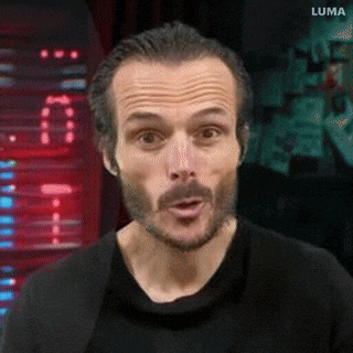 a man with a beard and mustache is making a surprised face while wearing a black shirt and a black jacket .