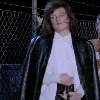 a woman in a white shirt and black jacket is standing in front of a chain link fence