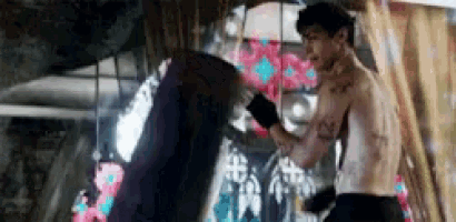 a man without a shirt is boxing with a woman in front of a graffiti wall .