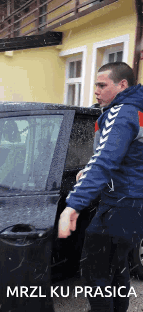 a man in a blue jacket is standing next to a car with the words mrzl ku prasica written below him