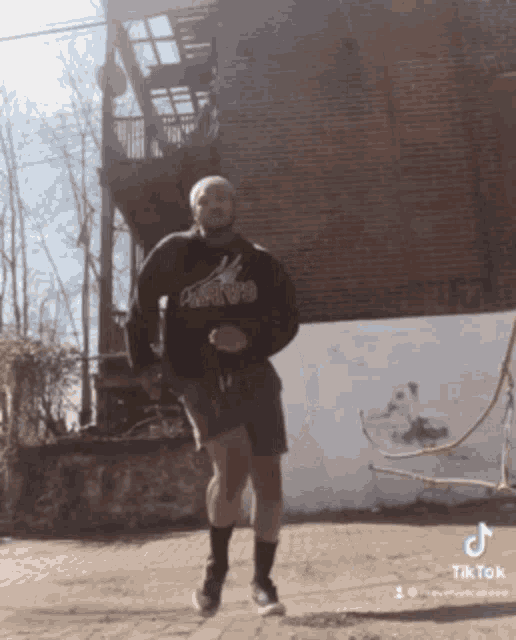 a man is jumping a rope in front of a brick building with a tiktok logo on the bottom right