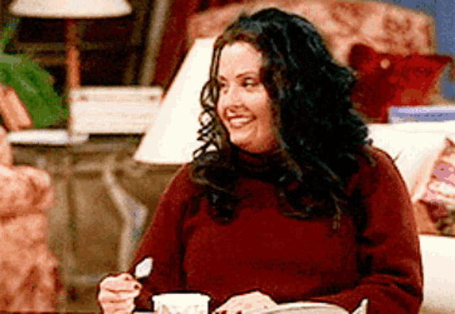 a woman in a red sweater is sitting at a table with a cup of coffee and a spoon .