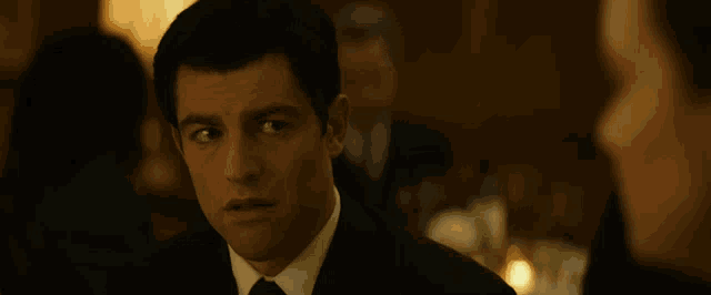 a man in a suit and tie looks at another man in a dark room