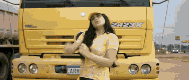 a woman stands in front of a yellow truck that says 2423k on the front