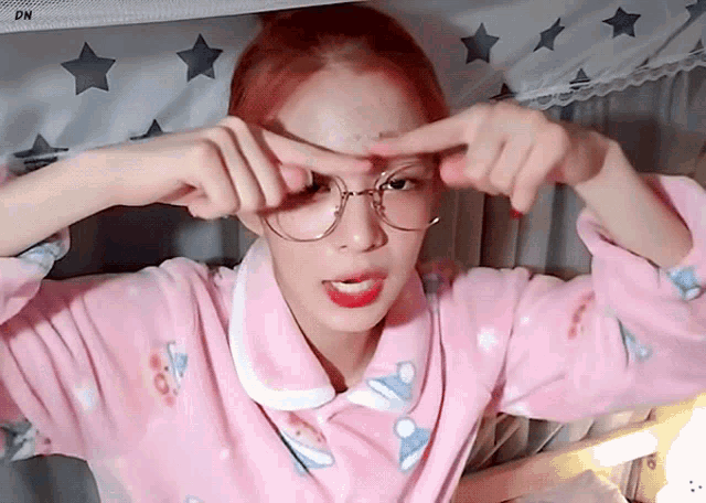 a woman wearing glasses and a pink pajama top is making a face