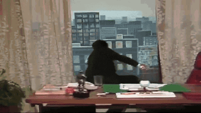 a man is sitting at a desk in front of a window looking out to a city