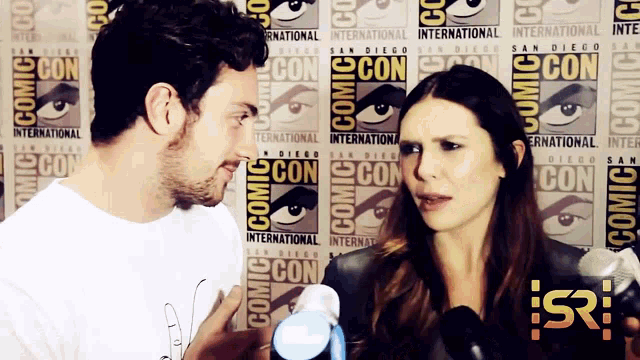 a man and a woman are talking in front of a wall that says comic con
