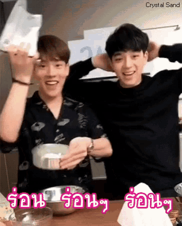 two young men are sitting at a table and one is holding a bag and the other is holding a bowl