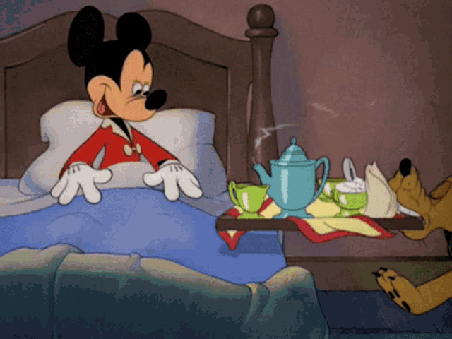 a cartoon of mickey mouse sitting on a bed next to a tray of tea