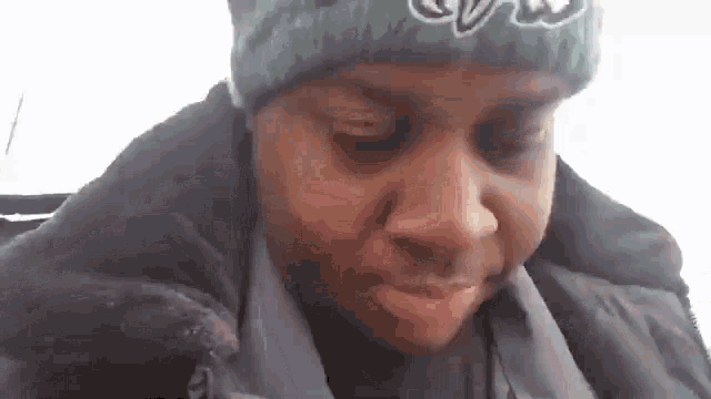 a man wearing a green beanie and a black jacket is looking at the camera .