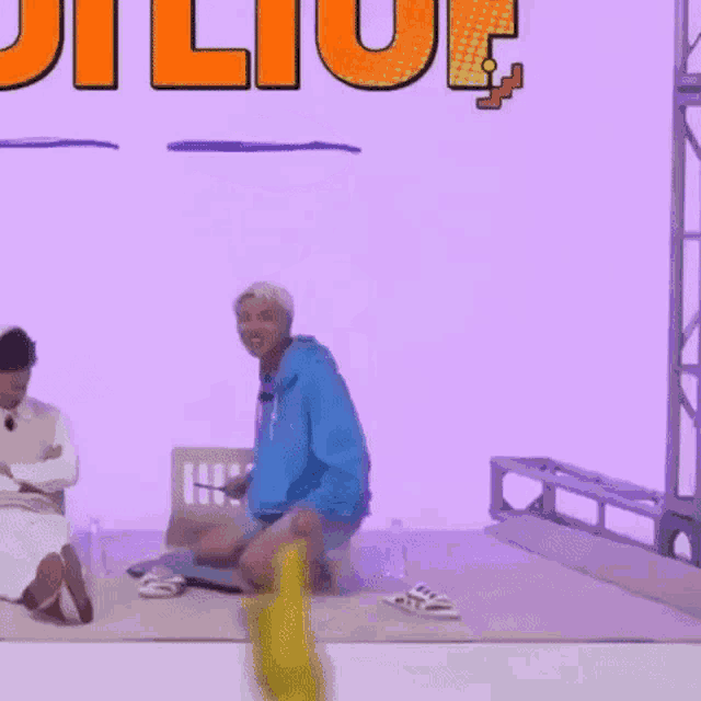 a man in a blue hoodie is kneeling down on the floor with a bottle of beer on his head .