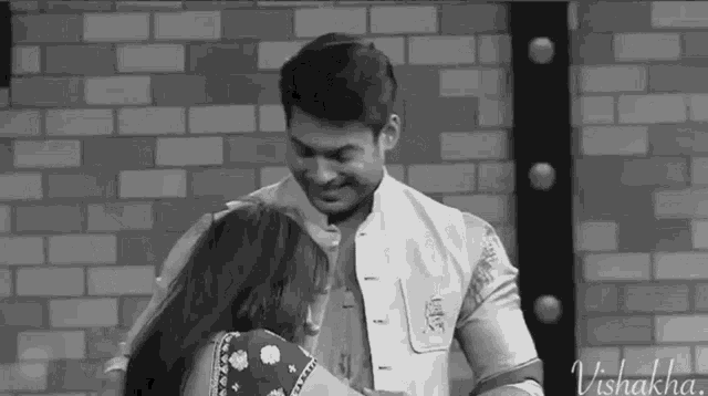 a man and a woman are hugging each other in front of a brick wall in a black and white photo .