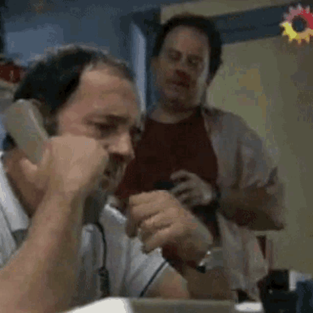 a man talking on a phone while another man stands behind him