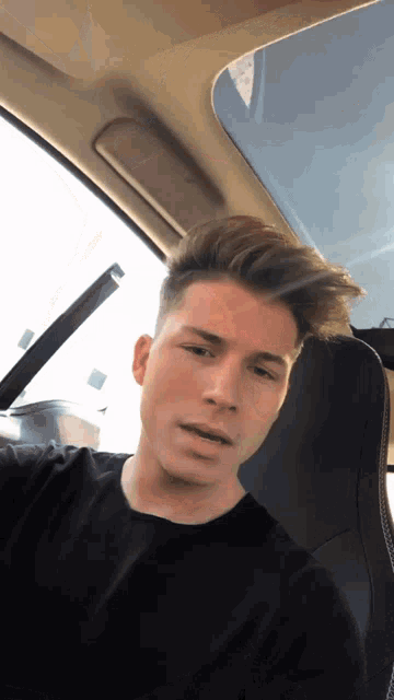 a young man in a black shirt sits in a car
