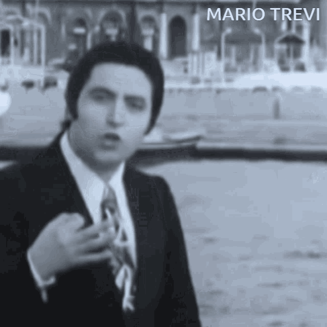 a man in a suit and tie is standing in front of a body of water with the name mario trevi on the bottom