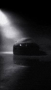 a black car is silhouetted against a spotlight in the dark