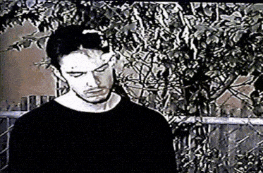 a man in a black shirt is standing in front of a chain link fence with trees in the background .