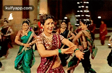 a woman is dancing in front of a crowd of people in traditional indian clothing .