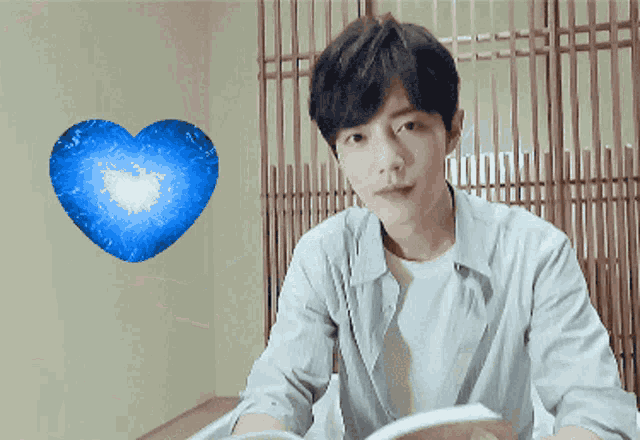 a young man is reading a book in front of a blue heart