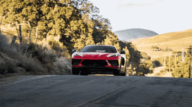 a red sports car is driving down a road with mountains in the background