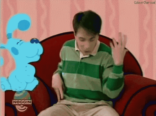 a man in a green and green striped shirt is sitting on a red chair next to a blue dog ..