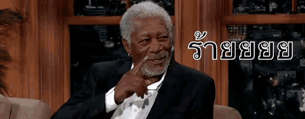 a man in a suit is sitting on a couch with a foreign language written on the bottom right