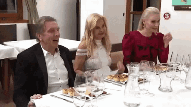 a man and two women are sitting at a table with plates of food and glasses of wine .