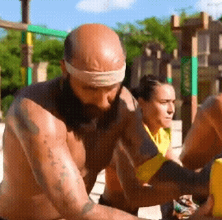 a man with a beard and a bandana on his head is lifting a yellow object while a woman looks on .