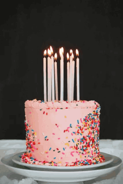 a pink birthday cake with candles and sprinkles