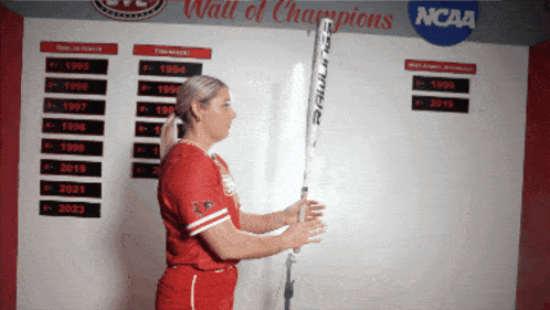 a woman holding a baseball bat in front of a wall of champions